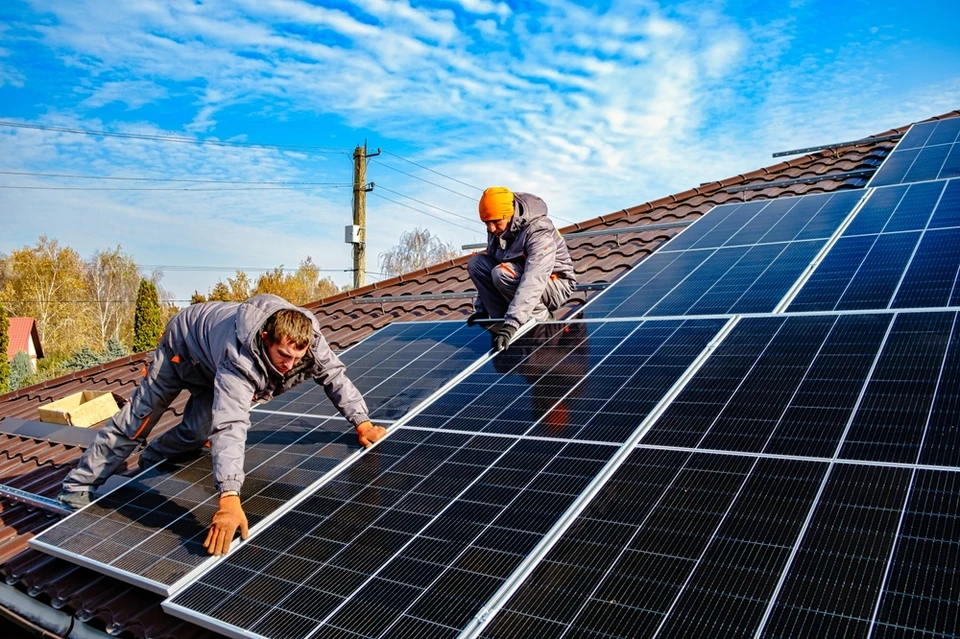 Deux techniciens installent des panneaux solaires photovoltaïques sur une toiture résidentielle en tuiles