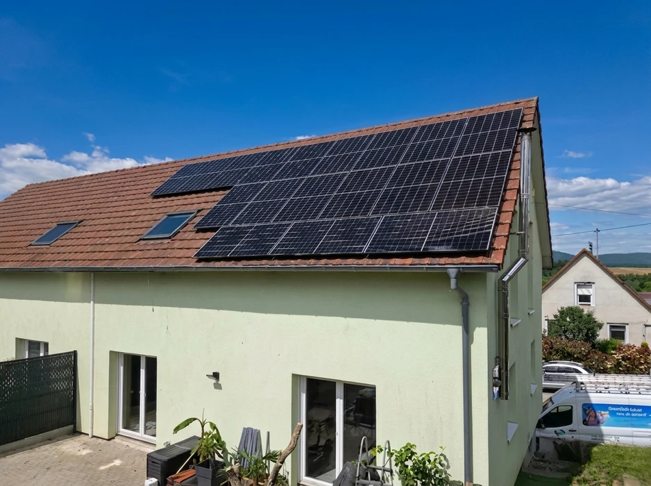 Maison individuelle avec toiture en tuiles rouges équipée de panneaux solaires photovoltaïques monocristallins noirs, disposés en plusieurs rangées