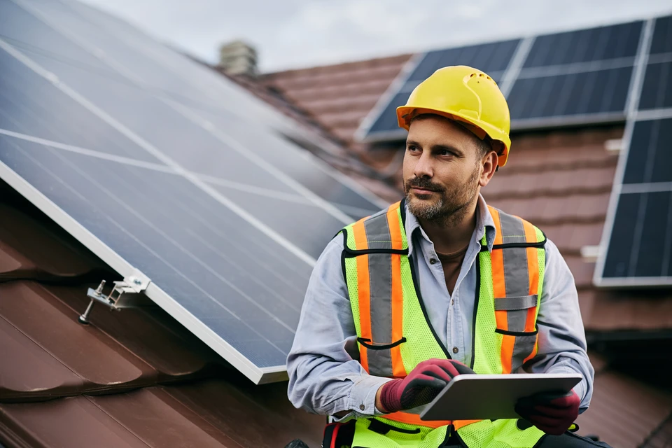 Ouvrier en équipement de protection individuelle avec casque jaune et harnais de sécurité travaillant sur installation de panneaux solaires photovoltaïques
