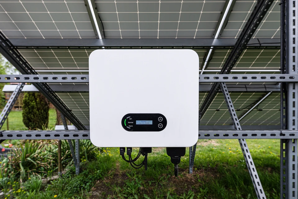 Photographie détaillée d'un onduleur photovoltaïque professionnel, montrant clairement l'appareil avec ses connecteurs et ses indicateurs lumineux, installé sur un mur ou un support dans un intérieur résidentiel ou commercial. L'onduleur doit être le sujet principal de l'image, photographié de manière à mettre en évidence sa construction robuste et ses caractéristiques techniques. L'éclairage doit être professionnel et la composition claire pour valoriser cet équipement central du système solaire.