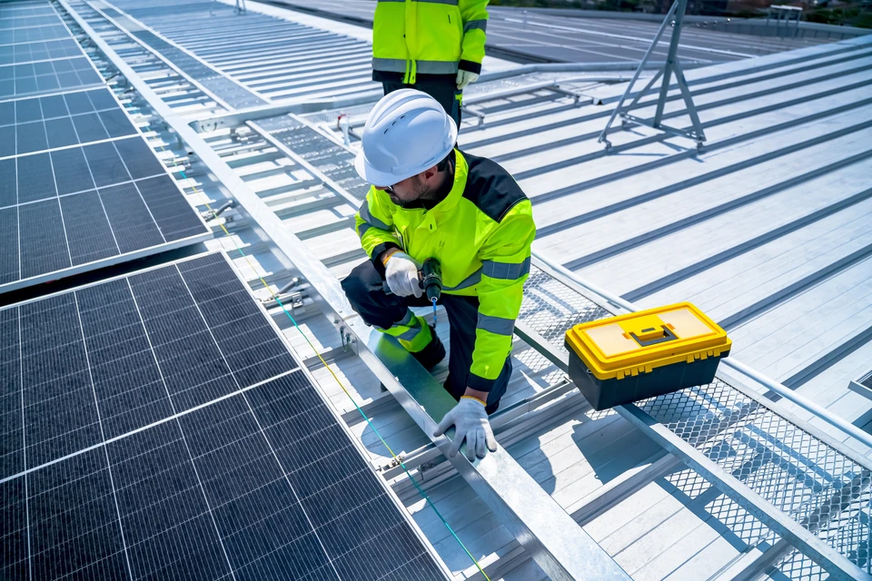 Deux techniciens installent des panneaux solaires photovoltaïques sur une toiture résidentielle en tuiles