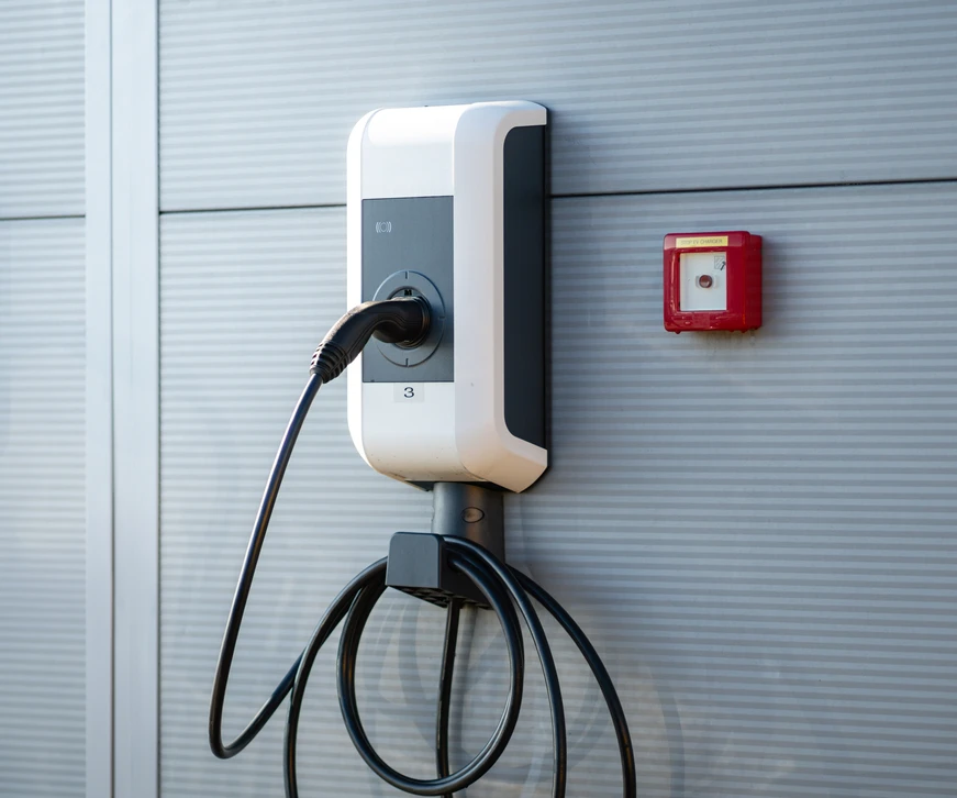 Ouvrier en bâtiment portant casque jaune et gants noirs installe ou répare un boîtier électrique blanc fixé au mur