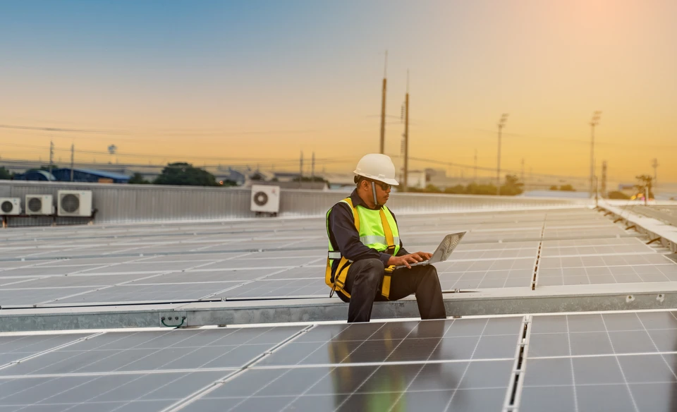 Ouvrier en équipement de protection individuelle avec casque jaune et harnais de sécurité travaillant sur installation de panneaux solaires photovoltaïques