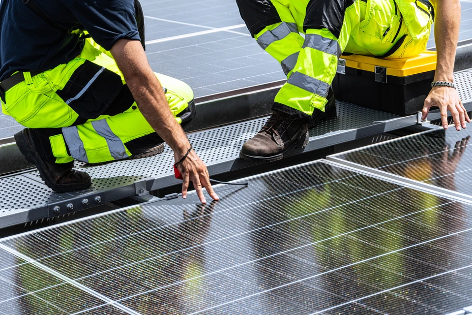 Ouvrier en équipement de protection individuelle avec casque jaune et harnais de sécurité travaillant sur installation de panneaux solaires photovoltaïques