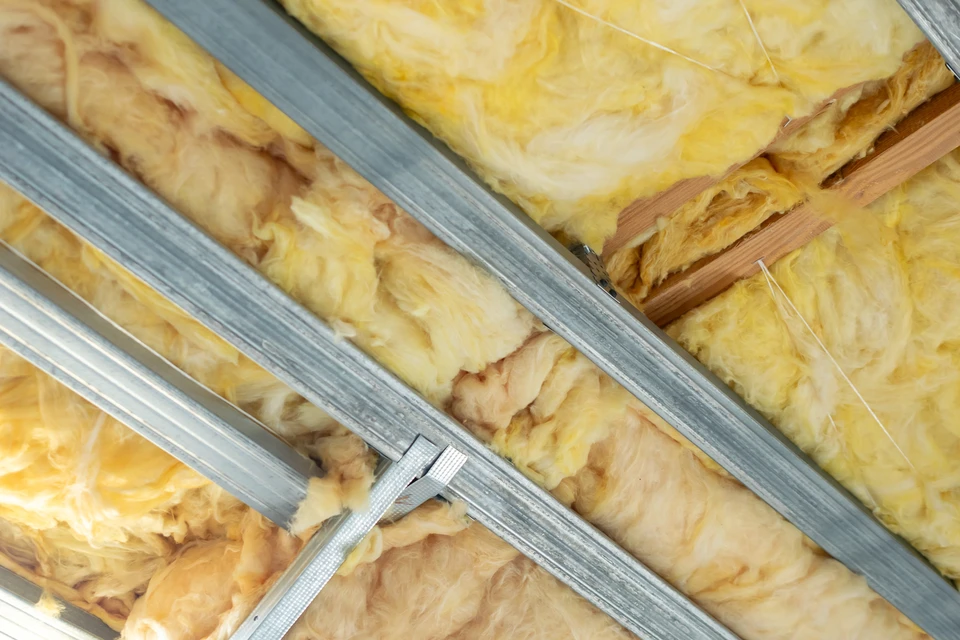 Une toiture résidentielle en cours de travaux montrant l'installation de panneaux solaires photovoltaïques sur une structure de toit en bois, avec un artisan en tenue de sécurité effectuant l'installation. La toiture doit être partiellement recouverte de panneaux solaires bleus/noirs, l'autre partie montrant la structure existante. Arrière-plan montrant une maison résidentielle en région rurale ou semi-urbaine.